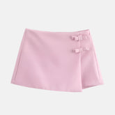 Saia curta rosa clara com design minimalista, detalhe de laços decorativos na lateral e corte assimétrico, ideal para um visual delicado e feminino.