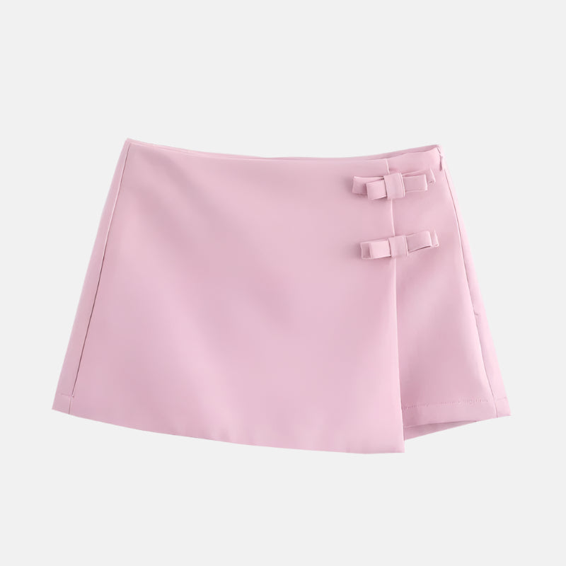 Saia curta rosa clara com design minimalista, detalhe de laços decorativos na lateral e corte assimétrico, ideal para um visual delicado e feminino.