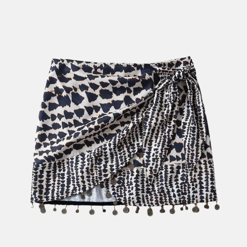 Saia curta com estampa geométrica em preto e branco, design envolvente com amarração lateral e detalhes de pingentes metálicos na barra, ideal para um estilo boho chic.