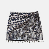 Saia curta com estampa geométrica em preto e branco, design envolvente com amarração lateral e detalhes de pingentes metálicos na barra, ideal para um estilo boho chic.