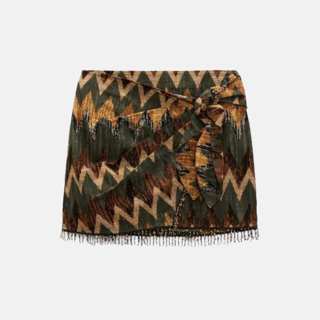 Saia curta com estampa geométrica em tons de verde, marrom e amarelo, detalhe de amarração na cintura e acabamento com franjas na barra, ideal para um visual boho chic.