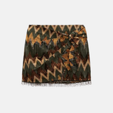 Saia curta com estampa geométrica em tons de verde, marrom e amarelo, detalhe de amarração na cintura e acabamento com franjas na barra, ideal para um visual boho chic.