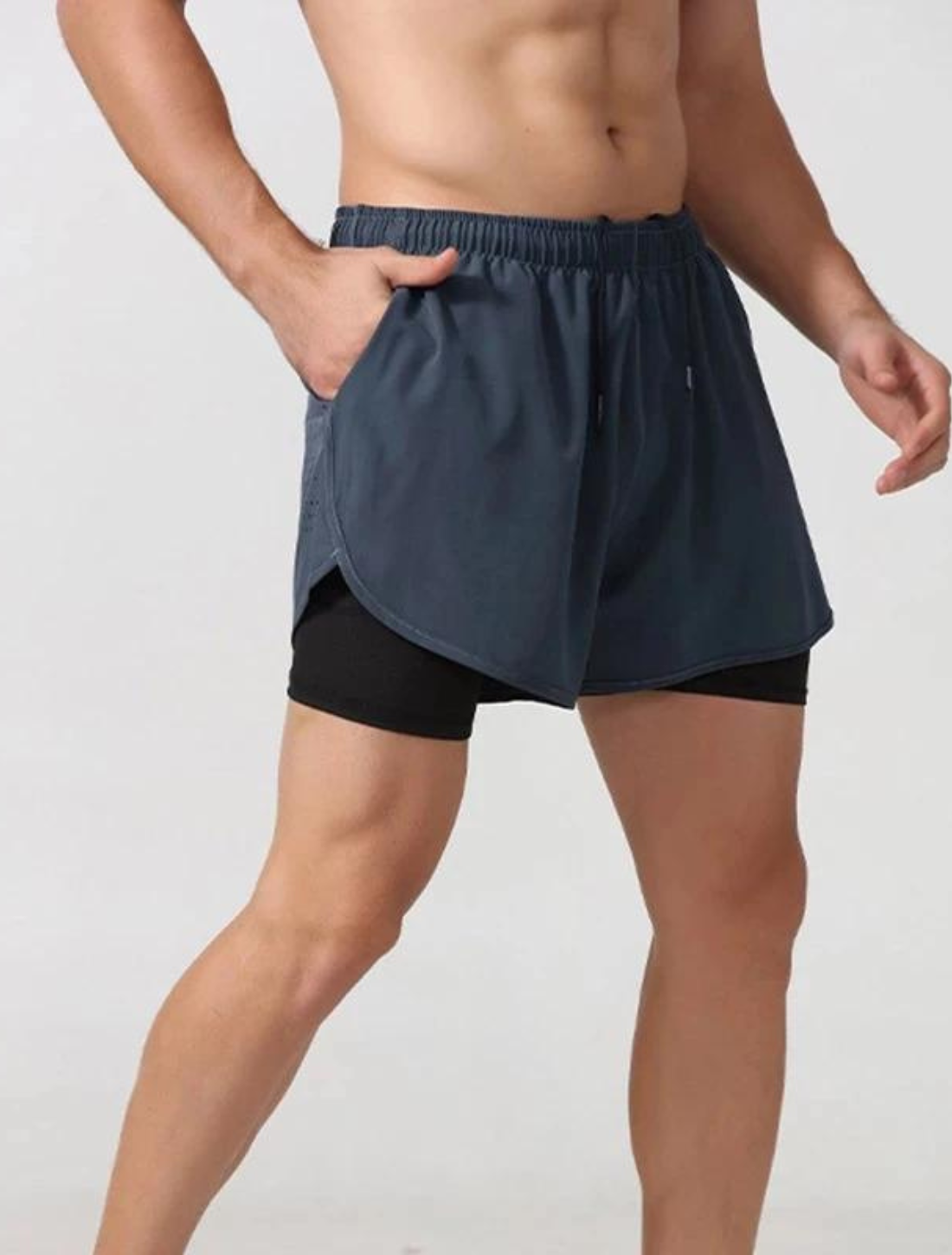 Homem vestindo o Short Urban Premium 2 em 1, com camada externa azul ventilada e camada interna de compressão preta. Ideal para treinos com conforto e suporte.