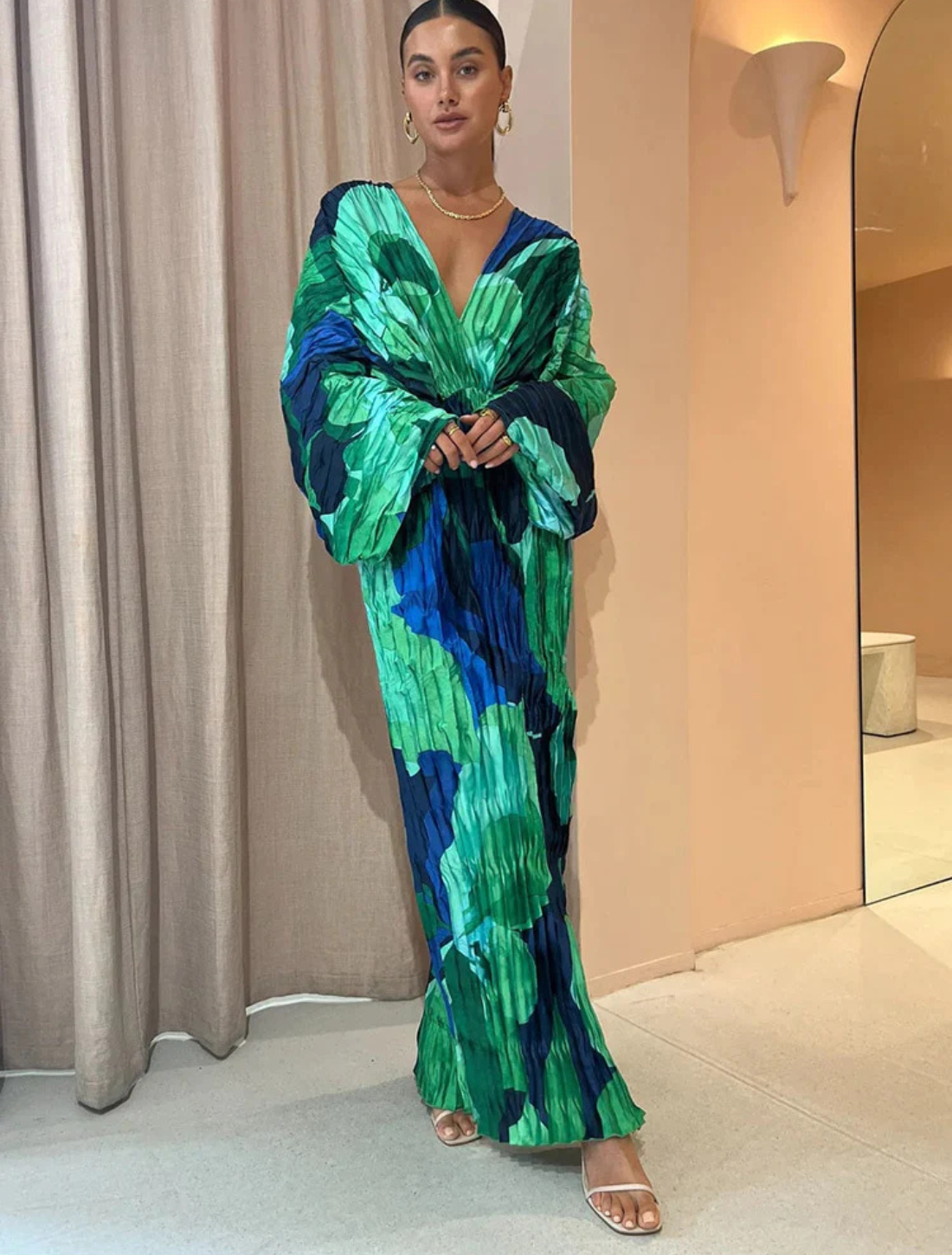 Vestido longo com estampa abstrata em tons de verde e azul, tecido plissado, mangas amplas e decote em V profundo, criando um visual elegante e moderno.
