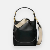 Bolsa bucket preta com acabamento em couro liso, costura contrastante branca, alça curta em couro e alça longa ajustável em tecido com detalhes dourados, ideal para um estilo casual e sofisticado.